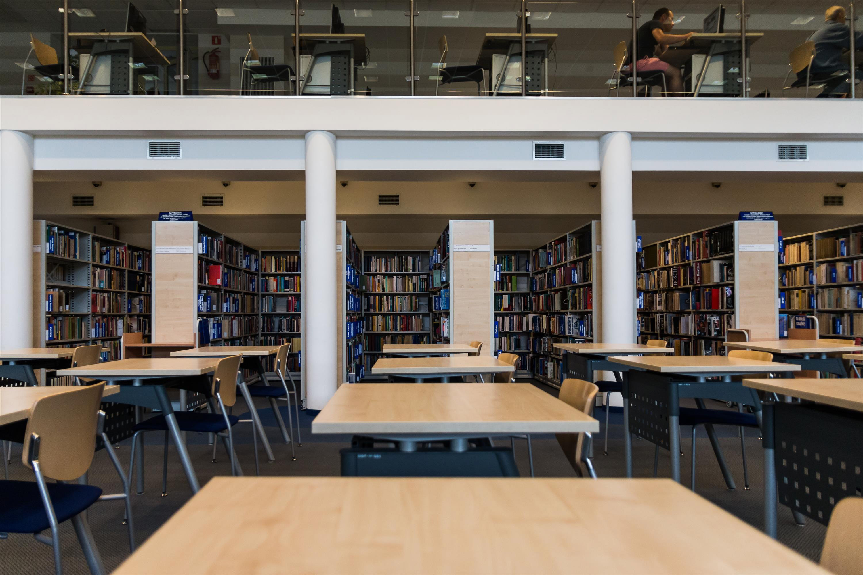 2 story library atrium.  The first floor is rows of books with individual tables , the second floor is all single table and chai