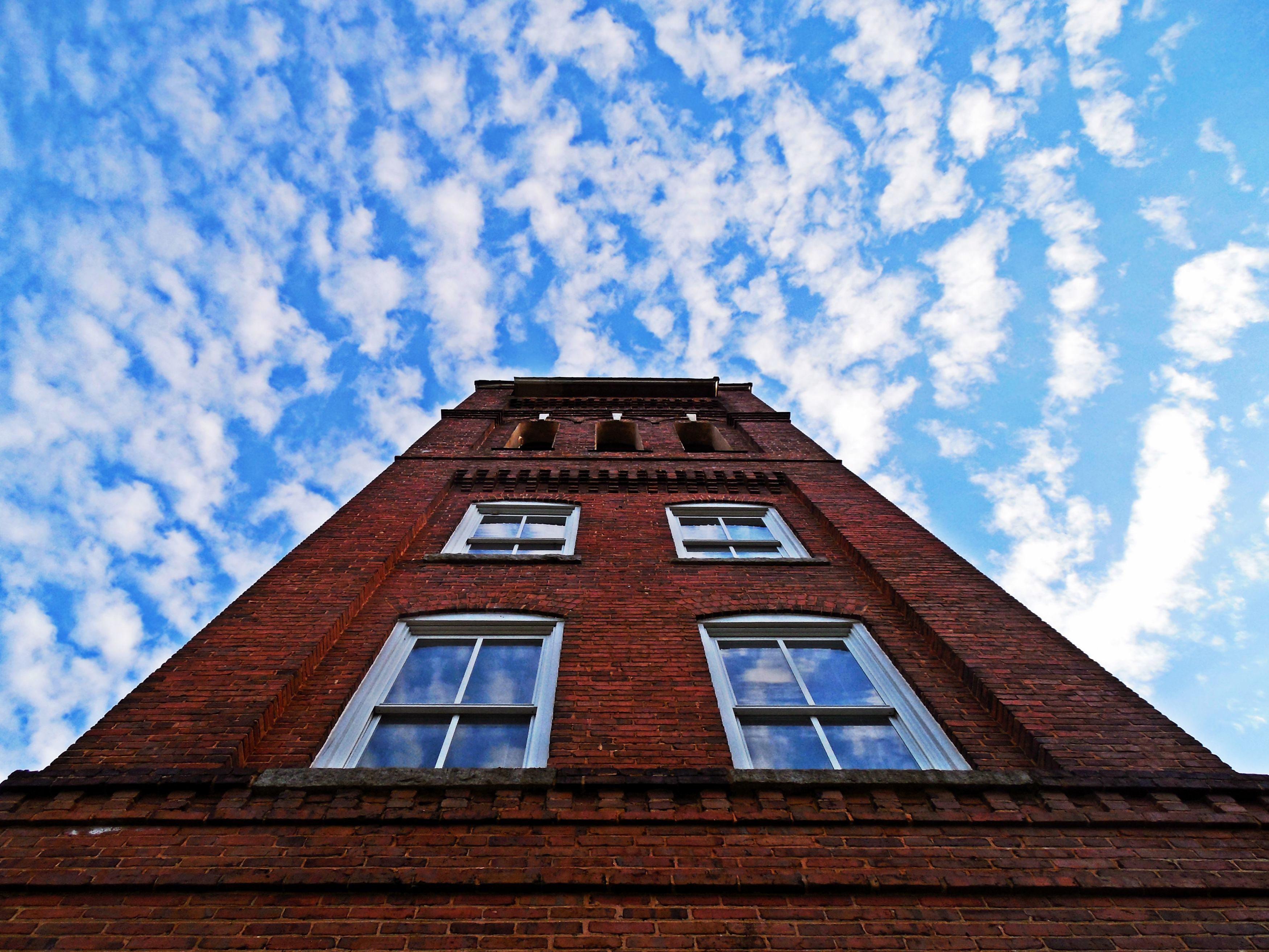 Looking up the face of a red brick building with a back ground of light wispy clouds against a blue sky