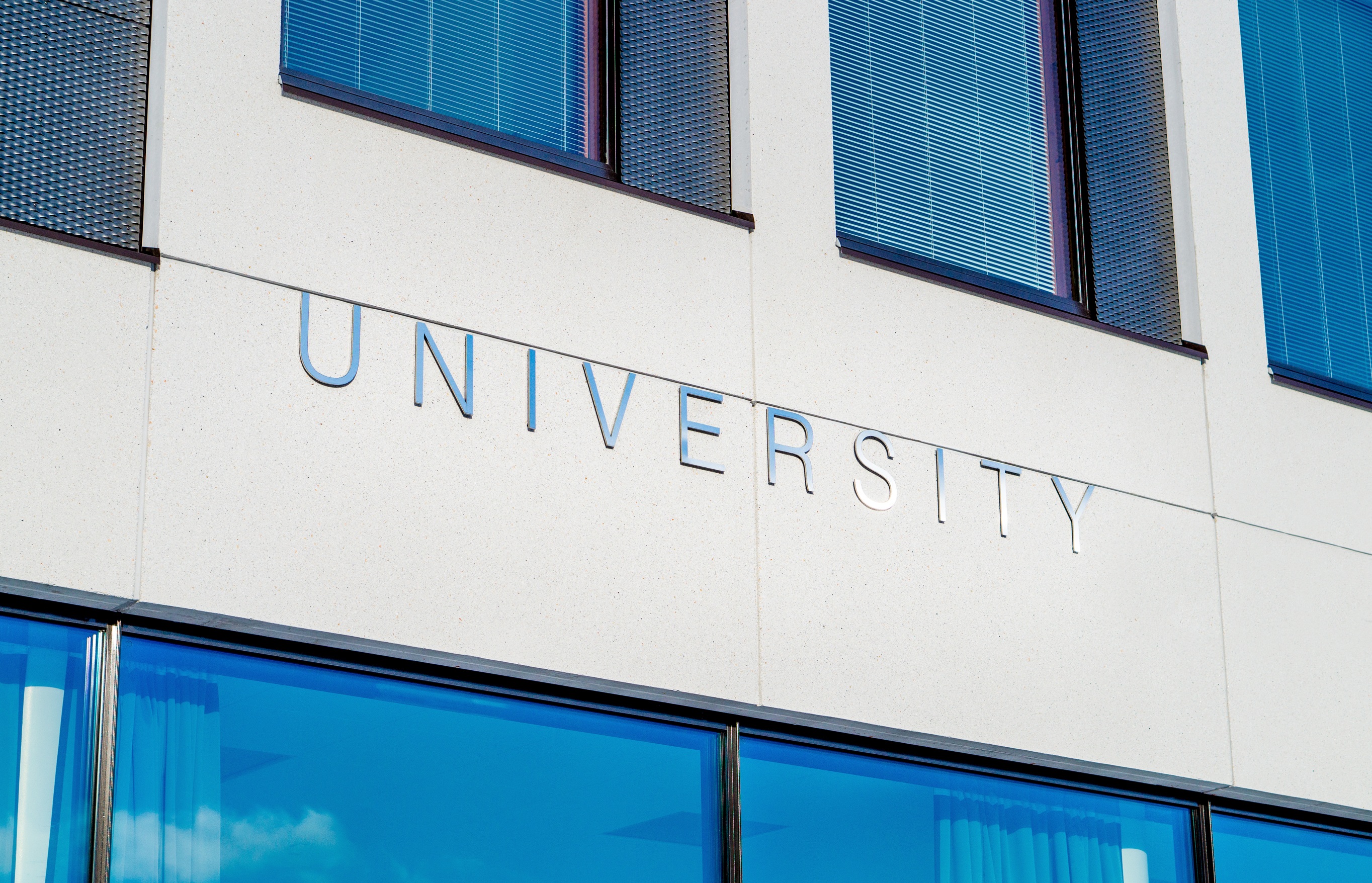 White faced building with large metallic letters spelling out "UNIVERSITY"