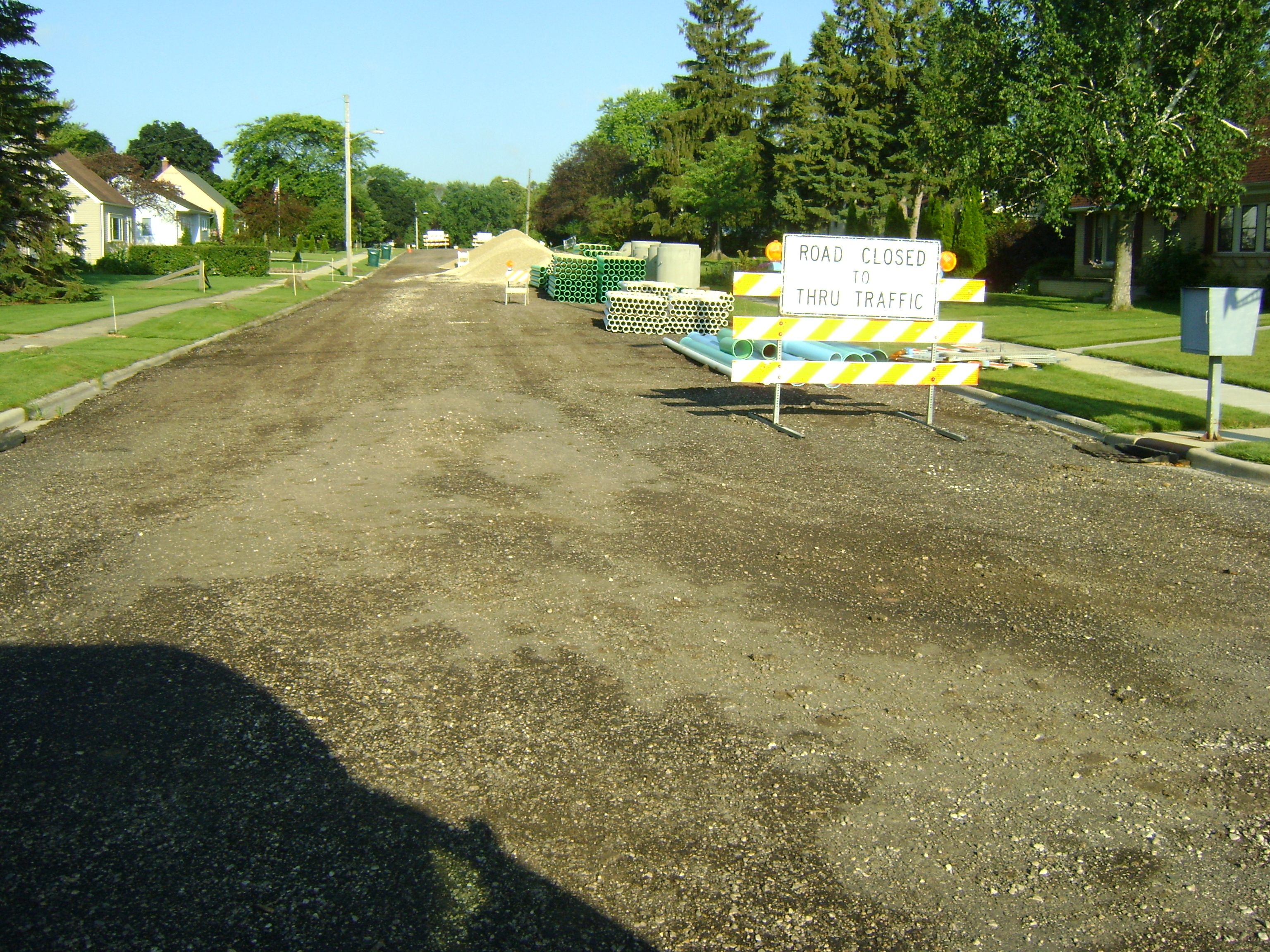 City of Kewaskum street under construction with a huge pile of green and white pipe waiting to be buried behind the Road Closed 