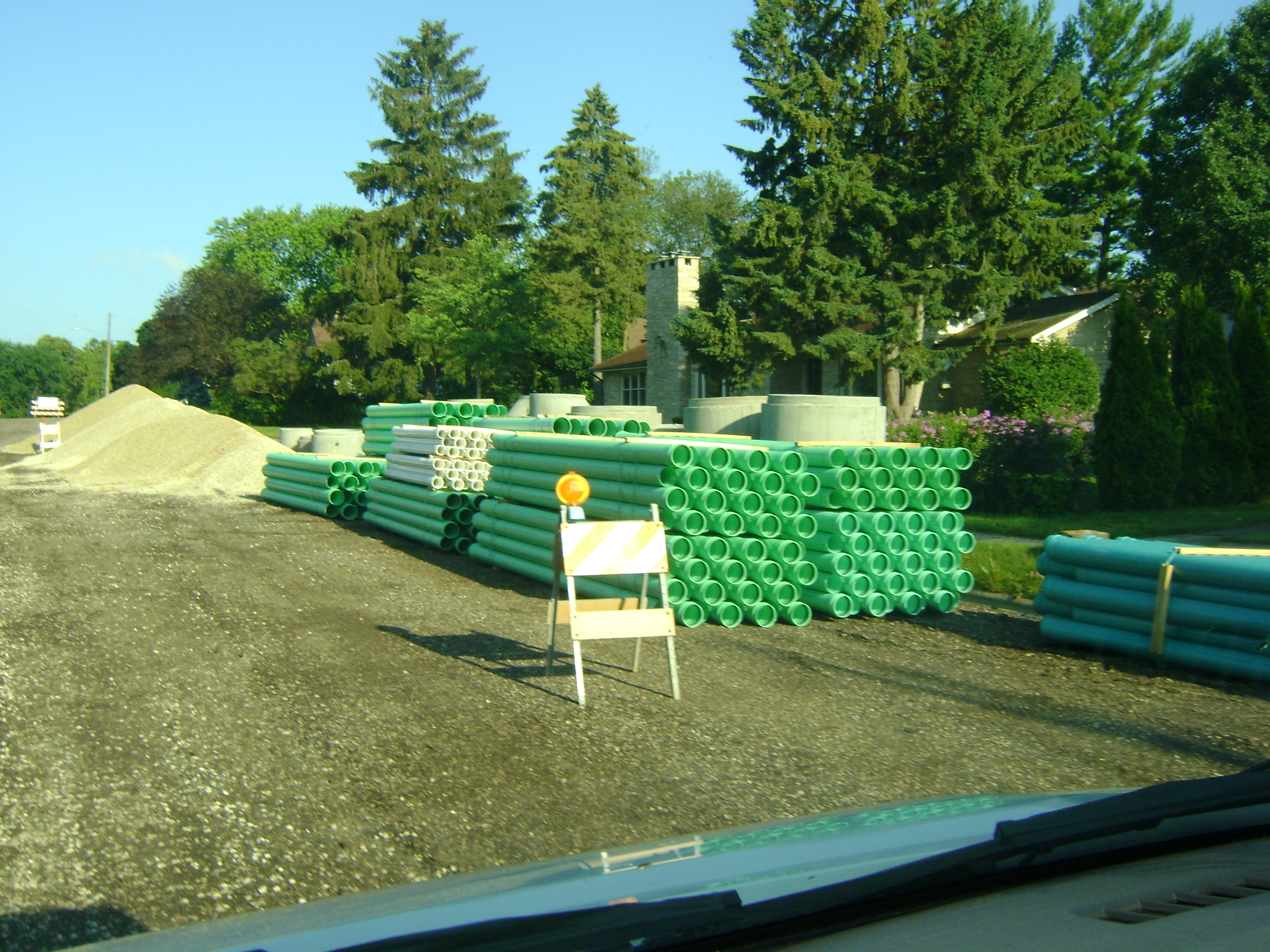 City of Kewaskum street under construction with a huge pile of green and white pipe waiting to be buried 