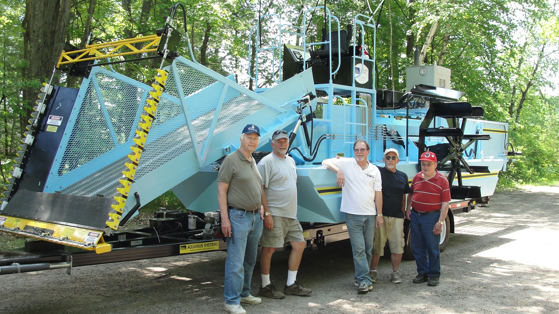 White River Lake District sky blue weed harvester on a trailer with the board members poised in front of it.